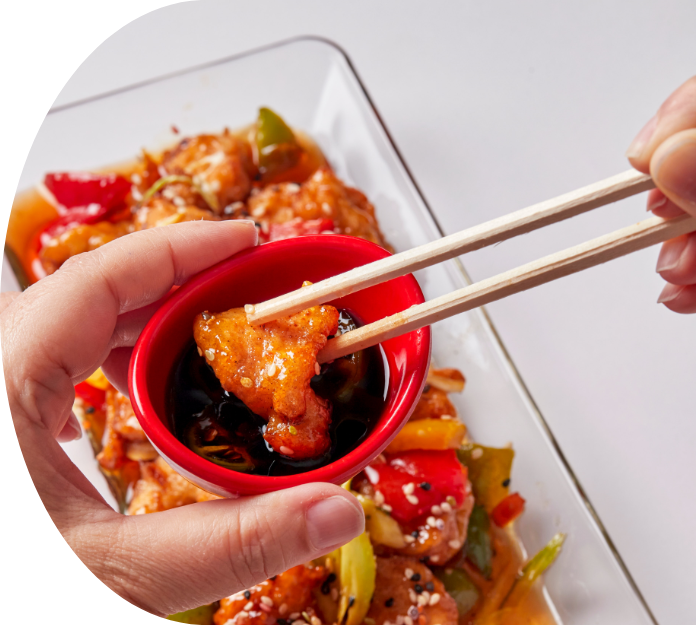 tso's chicken held by chopsticks and being dipped in sauce